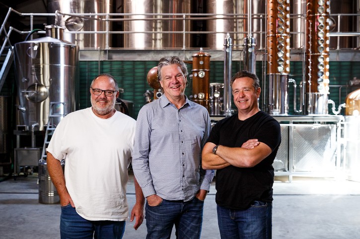 Three friends stand in front of a large distiller: Matt Giudice, John McVeigh and Jason Townes