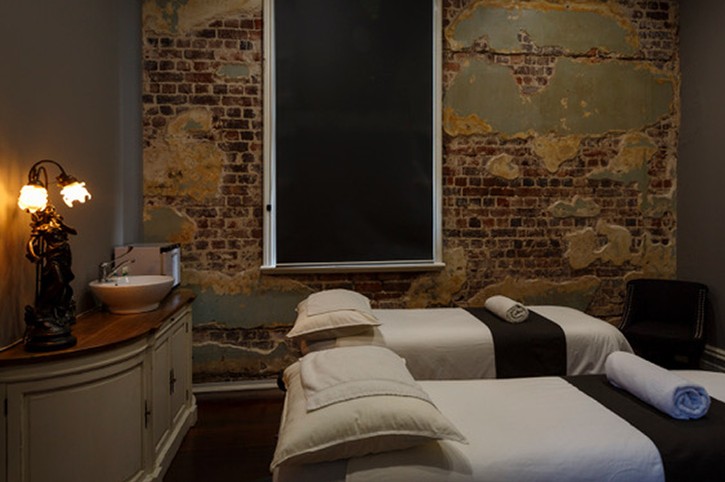 two beds with white linen in boutique day spa with vintage lighting and exposed brick wall