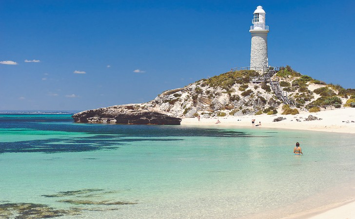 white lighthouse stands tall on rugged hill above clear, turquoise bay