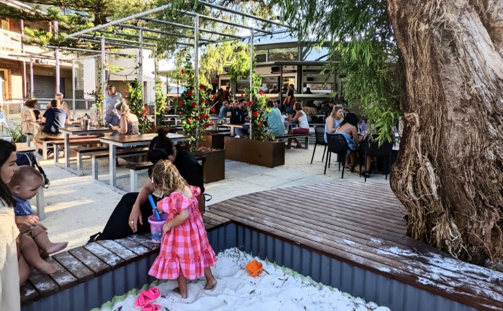 children play in sandpit in beer garden with green vines making a canopy