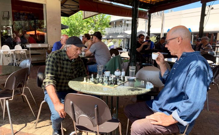 two people sip coffee and play a board game at table and chairs outside cafe