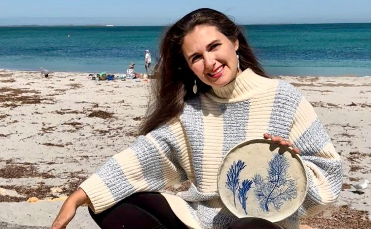 person hold hand crafted ceramic plate in front of blue sky, turquoise ocean and white sands