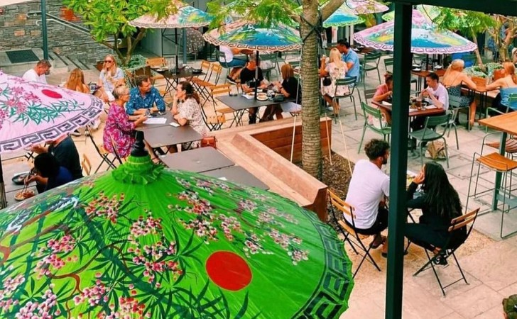looking down through colourful umbrellas in lush courtyard where people are chatting and dining