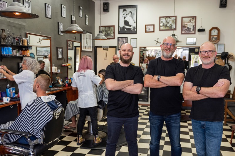 three bearded blokes, with arms crossed, stand in a barber shop