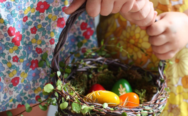 children's hands hold hand woven easter basket filled with colourful eggs