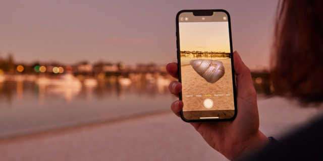 person holds phone displaying AR against coast scape at dusk