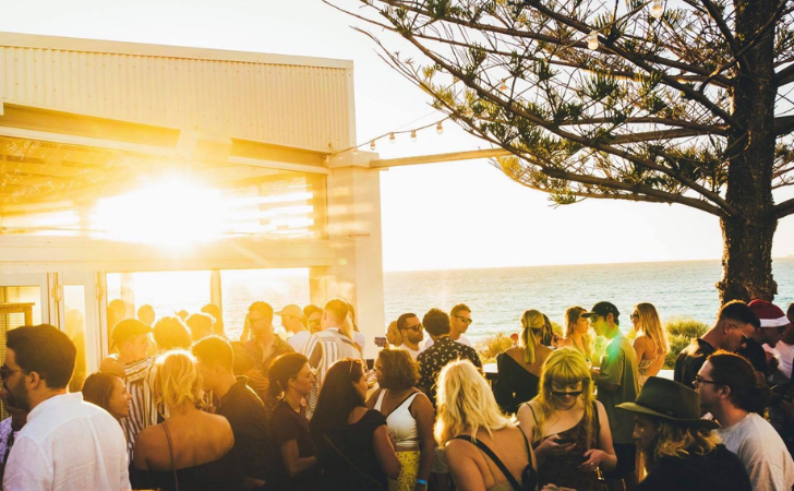 Coast Port Beach crowd in al fresco space while sun sets in the background