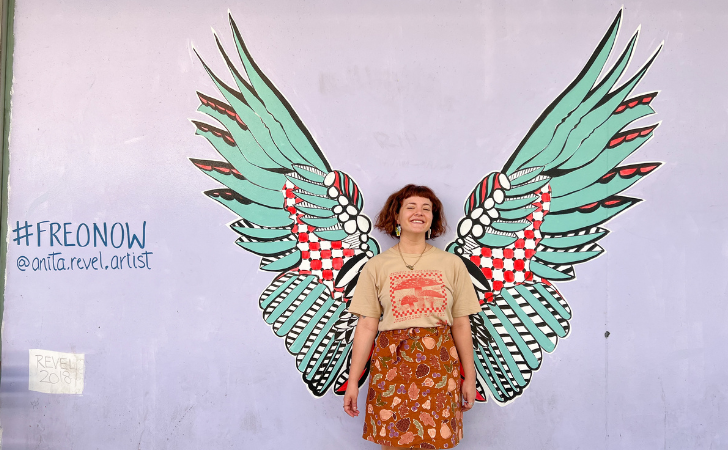 person stands in front of beautiful, green painted wings on a purple wall