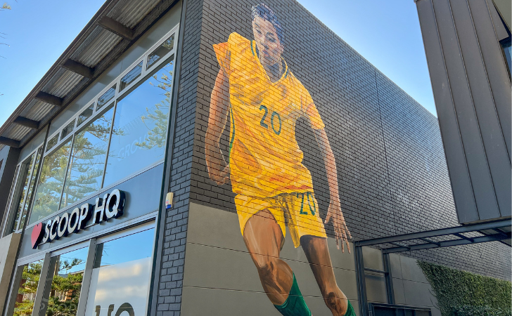 Mural of Sam Kerr in green and gold matilda's kit spans the height of a building