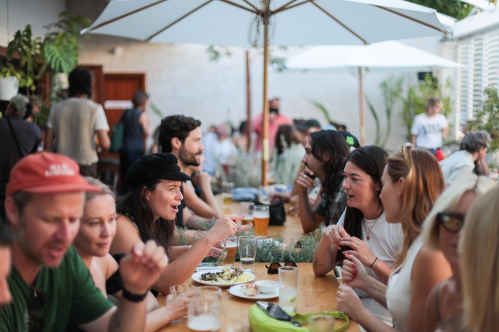 Patio Bar - guests eating food and enjoying drinks at a long wooden table under a white umbrella