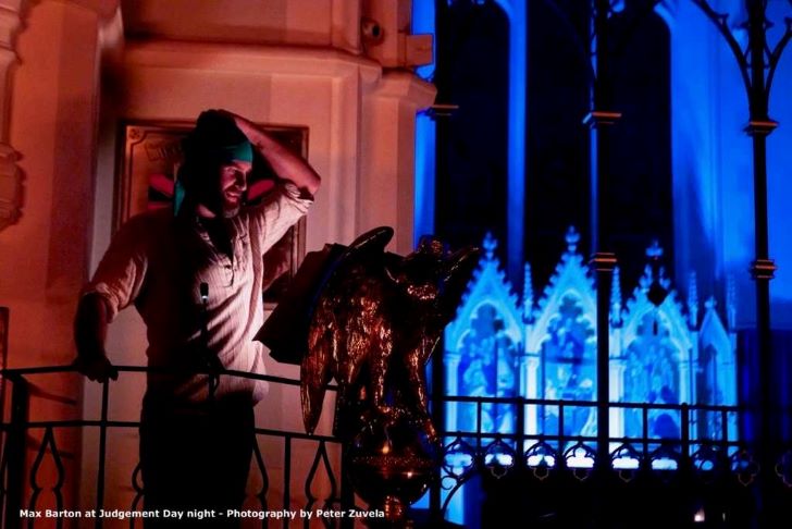 A man performs in a dark room with blue light and heritage architecture.