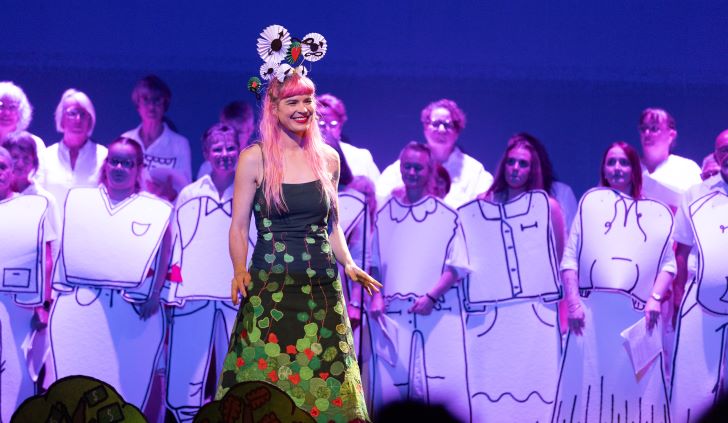 A girl in a green dress performs in front of a choir.