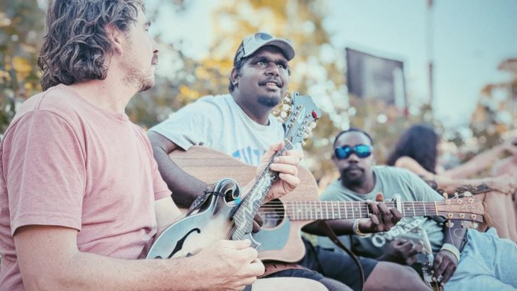 Two men play guitars on a sunny day.