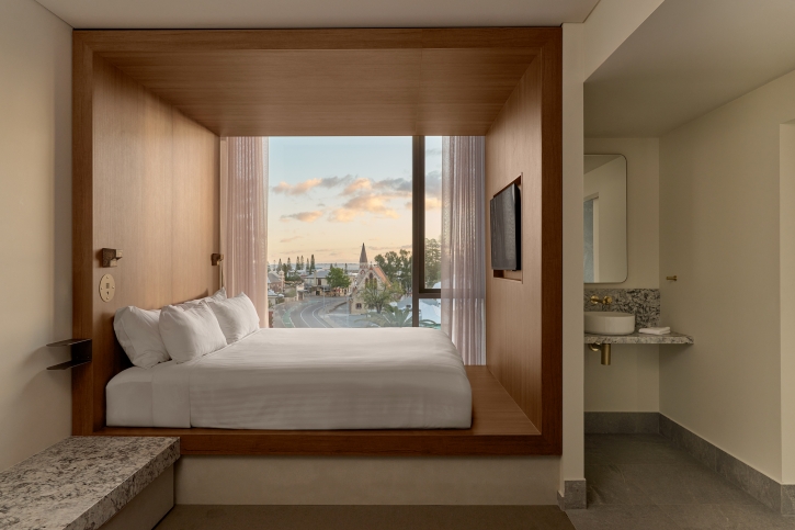 A plush hotel bed in front of a floor to ceiling window overlooking a city.