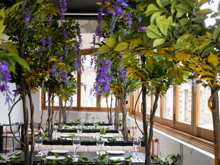 A restaurant dining room with lush green and purple foliage overhead.