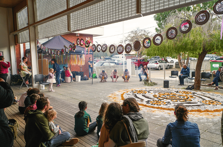 a cultural celebration with Aboriginal dancers and a didgeridoo with a design on the ground and children and families watching