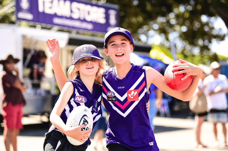 two kids out front of the Freo Dockers game in purple Dockers gear and holding an AFL ball in Fremantle, WA 
