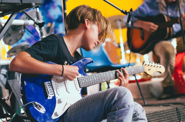 young boy playing a blue electric guitar on a stage