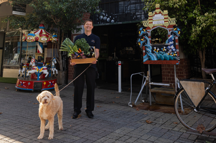 a man and a dog standing outside the Fremantle markets, the man has a basket of goods in his arms