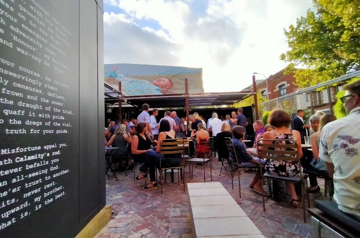 Large group of adults enjoying drinks in the courtyard of Calamity's Rod