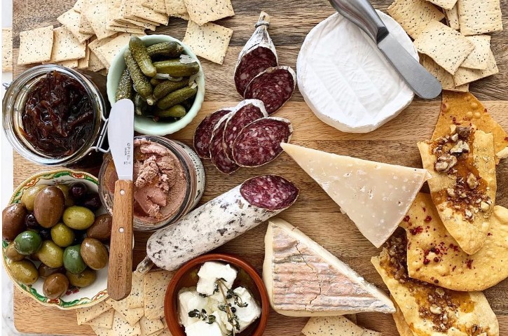 Platter of gourmet cheese, olive, deli meats on wooden board