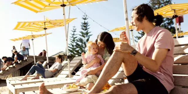 family eating fish and chips at Bathers Beach on sun loungers under yellow umbrellas
