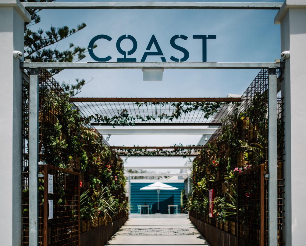 Main entrance gate at Coast Port Beach Fremantle lined with shrubs and sign over the gateway
