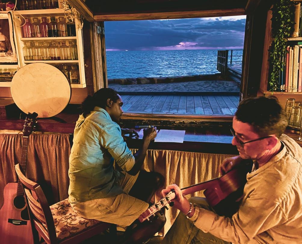 two men sitting playing guitar and writing