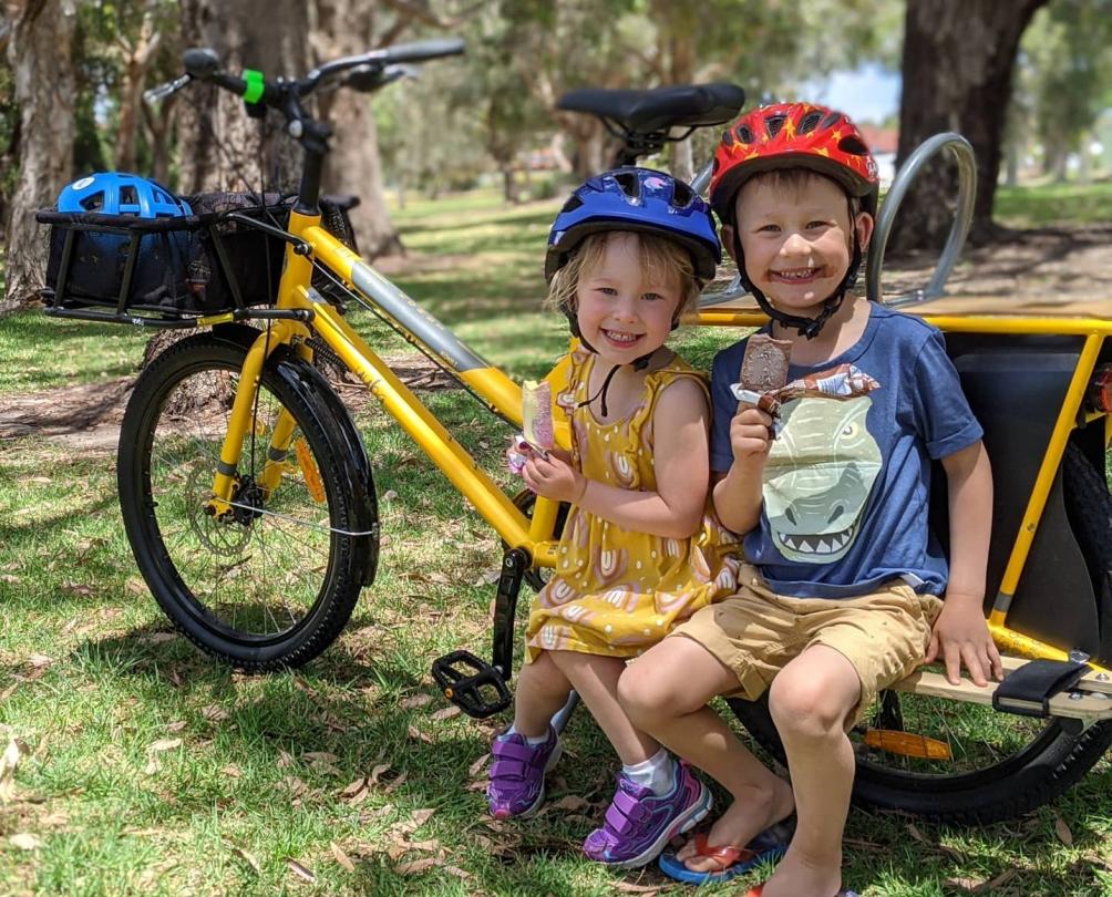 Two children on a cargo bike eating ice creams