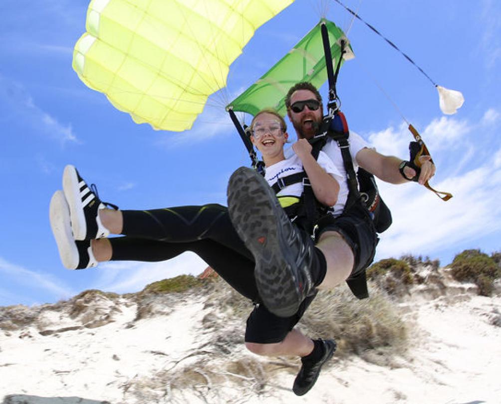 woman and man using a parachute to land on a beach at rottnest island