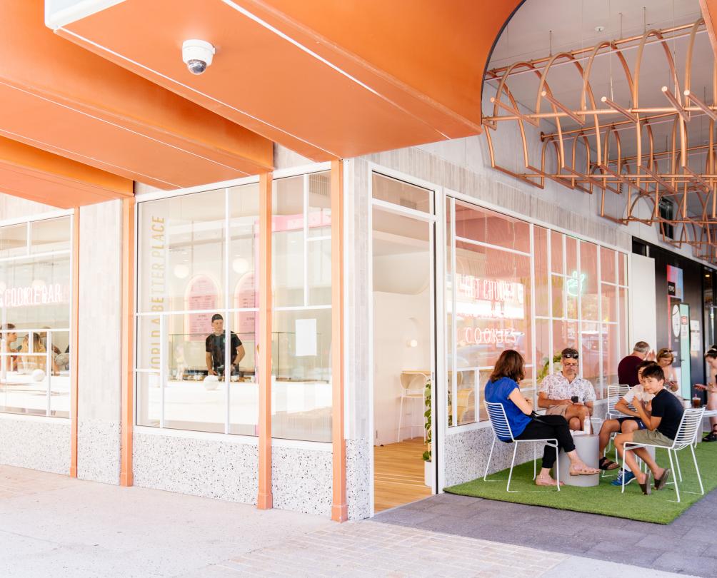 Exterior of Get Chunky retail store. Group of people seated eating cookies under the orange colour awning of the FOMO building