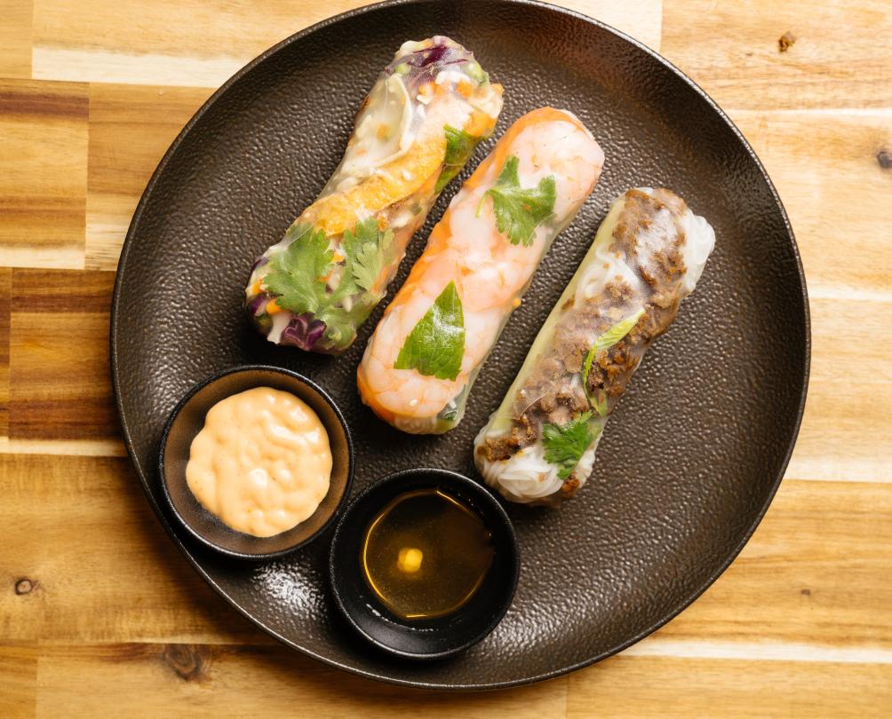 Assorted rice paper rolls from Rolld presented on brown plate with dipping sauces