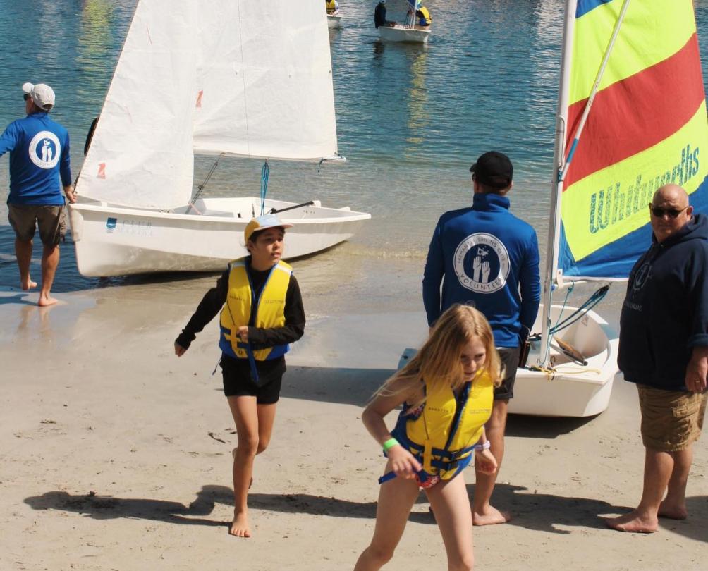 two children in yellow life jackets walking along the beach after exiting from a small yacht.