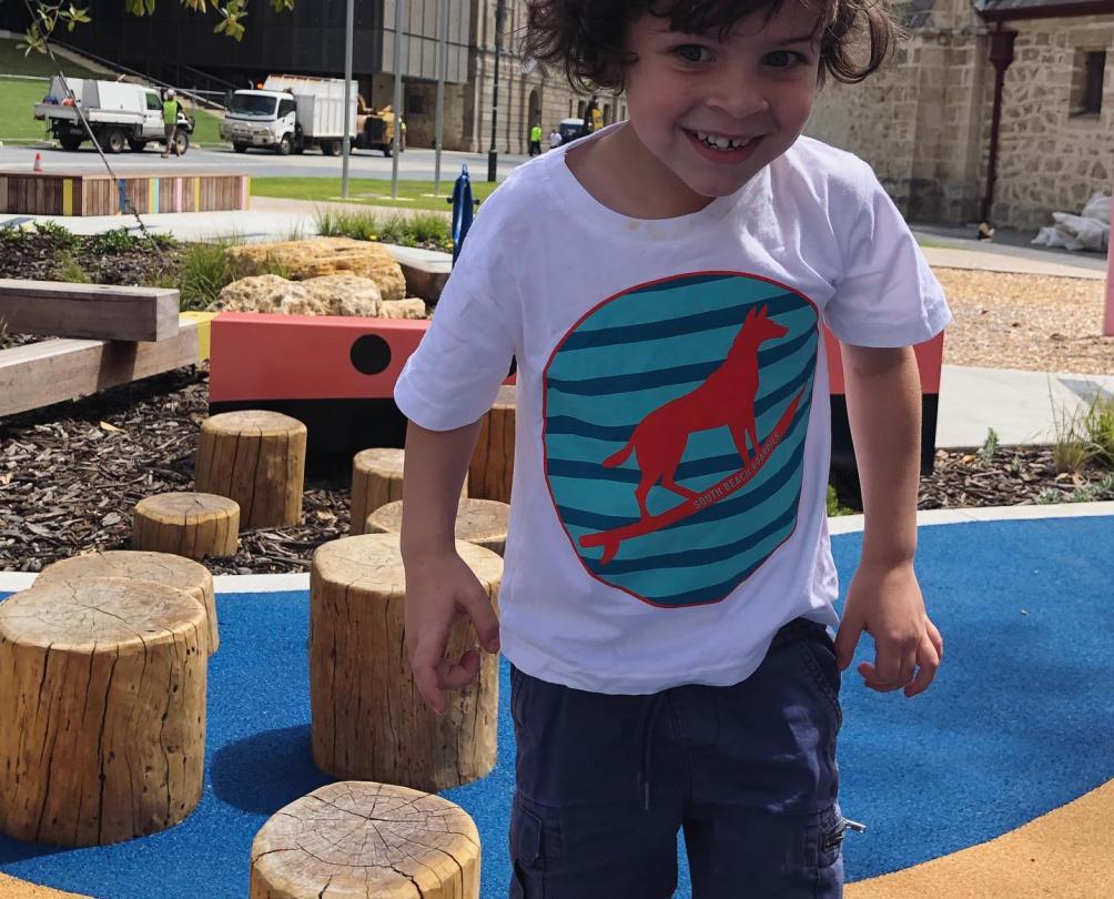 child playing in playground with t-shirt featuring the dingo flour logo on it.  