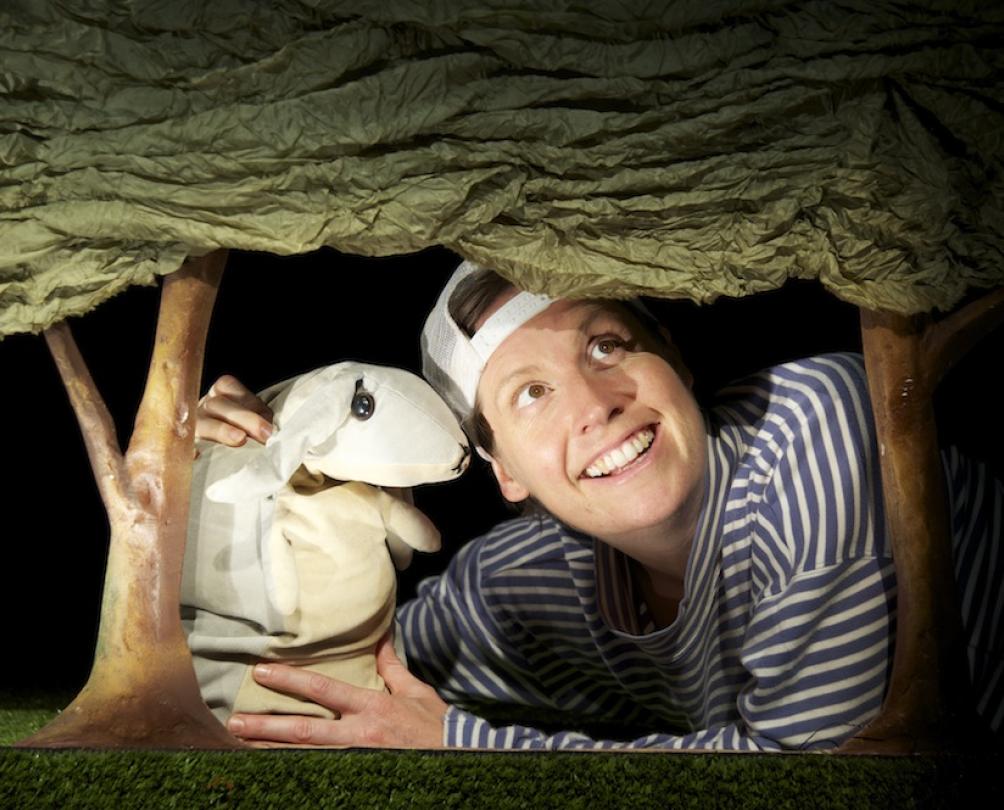actor wearing a backwards baseball cap holding a rabbit puppet on a stage 