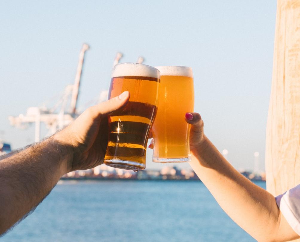 two hands cheers beers with the Fremantle cranes in the background