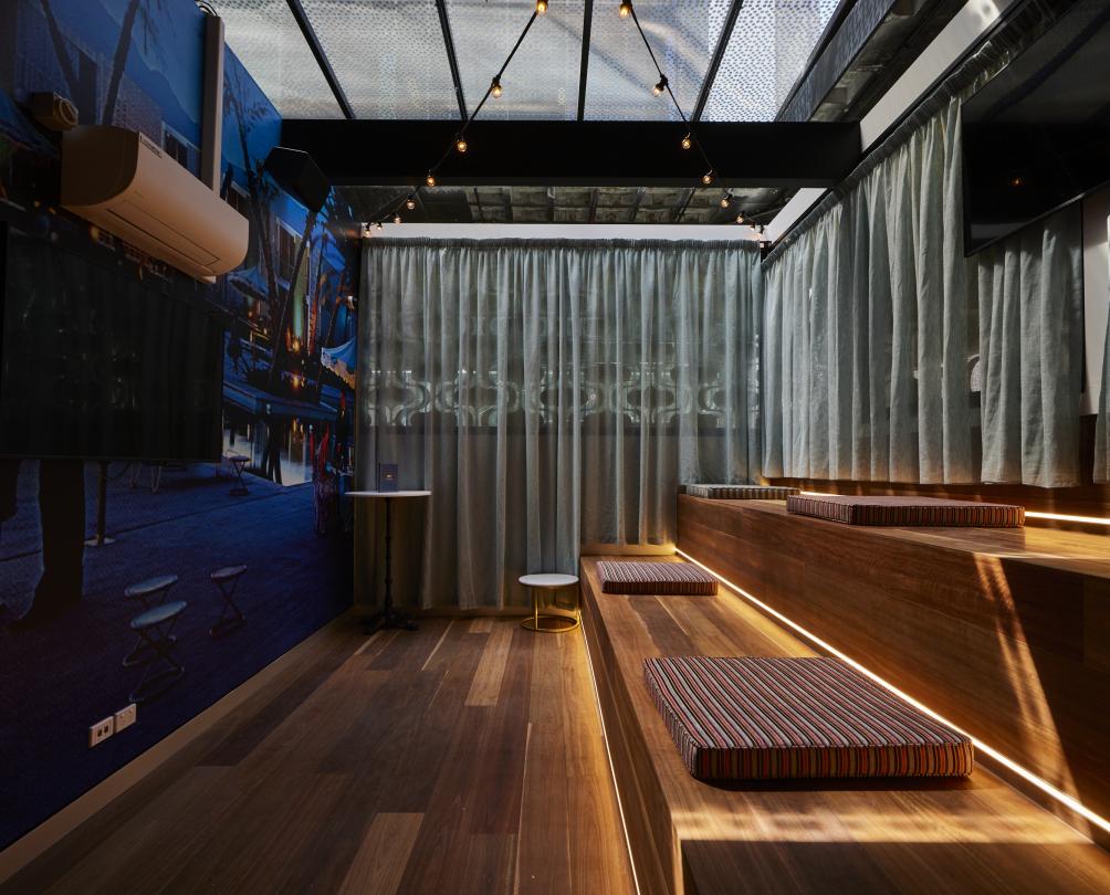 Party room at Strike Fremantle with wooden atrium style seating, stripey cushions, and a blue, streetscape feature wall