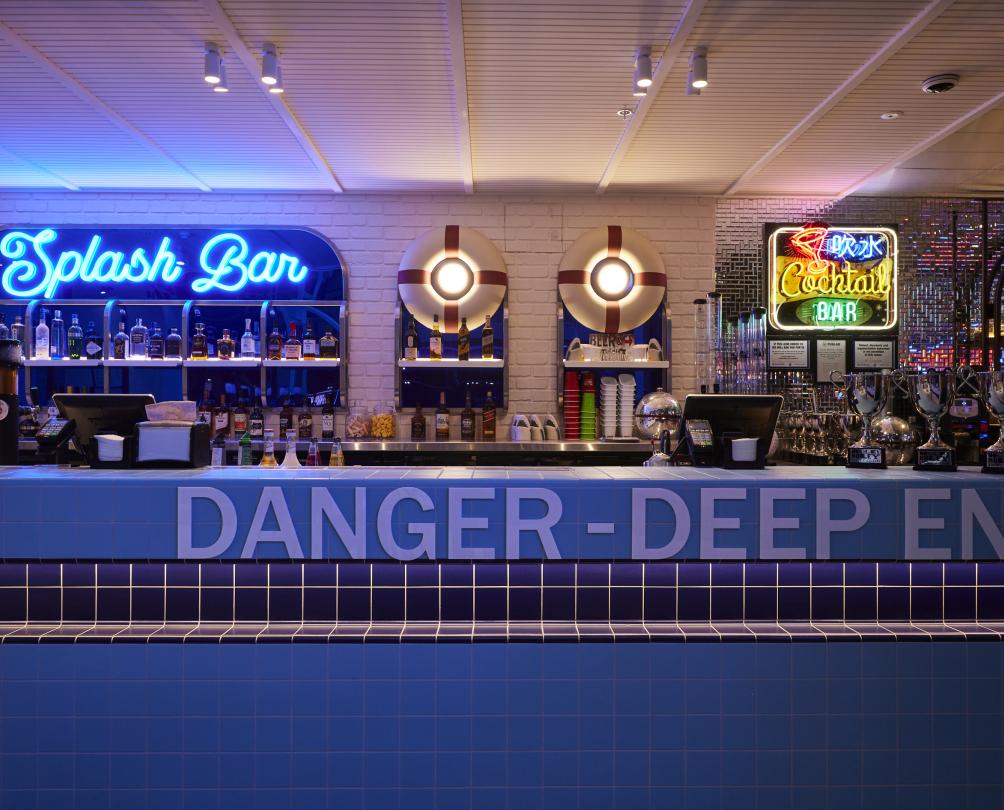 Splash Bar at Holey Moley with neon signs behind the bar, spirit bottles and "DANGER, DEEP END" painted on the side of the ar