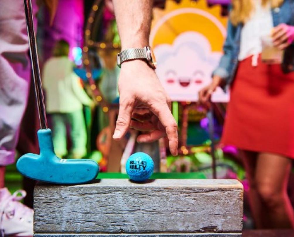 Man's hand reaching for a blue golf ball at Holey Moley 