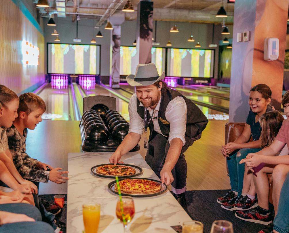 Kids being served up pizzas at Strike Bowling with the bowling lanes in the background