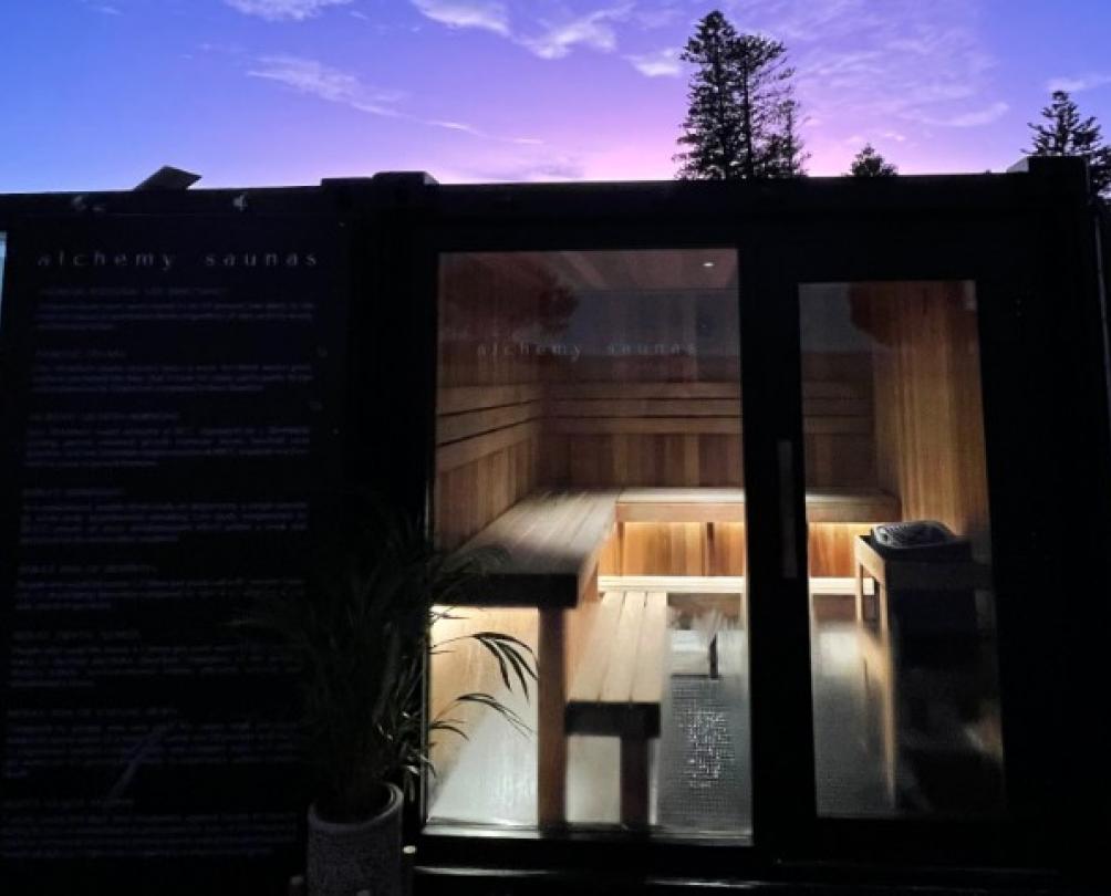 beach side sauna sits, illumminated, in front of purple dusk sky