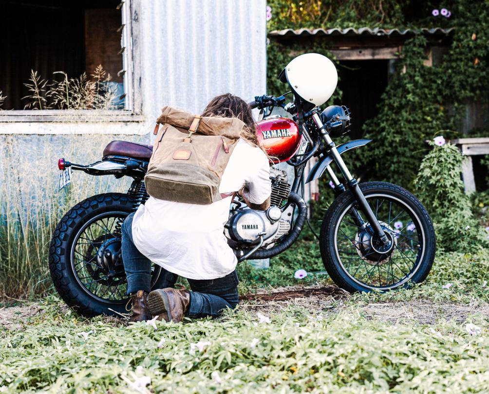 Man crouching in front of a motorcycle parked outside a iron shed