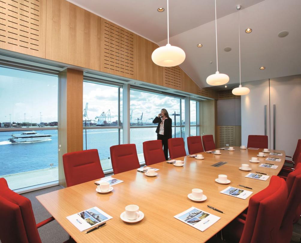 Large boardroom table lined on either side with red office chairs in front of windows overlooking Fremantle Harbour