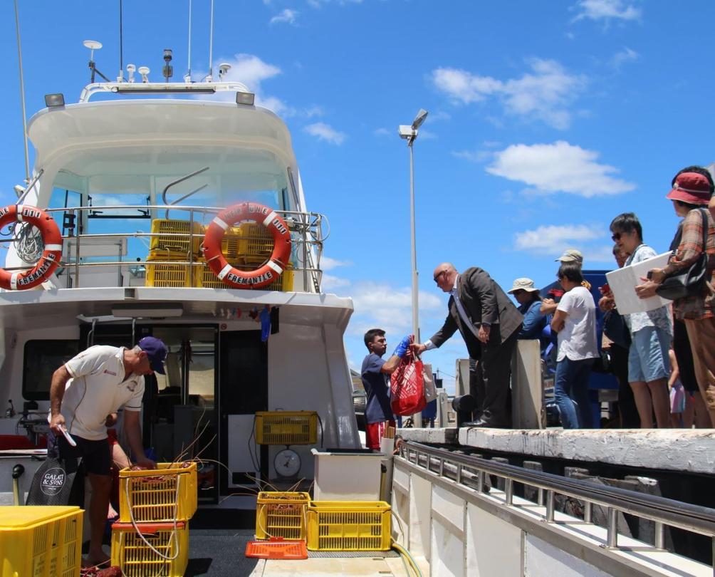 fishermen pass freshly caught lobsters to customer from boat docked at Fremantle Fishing Boat Harbour