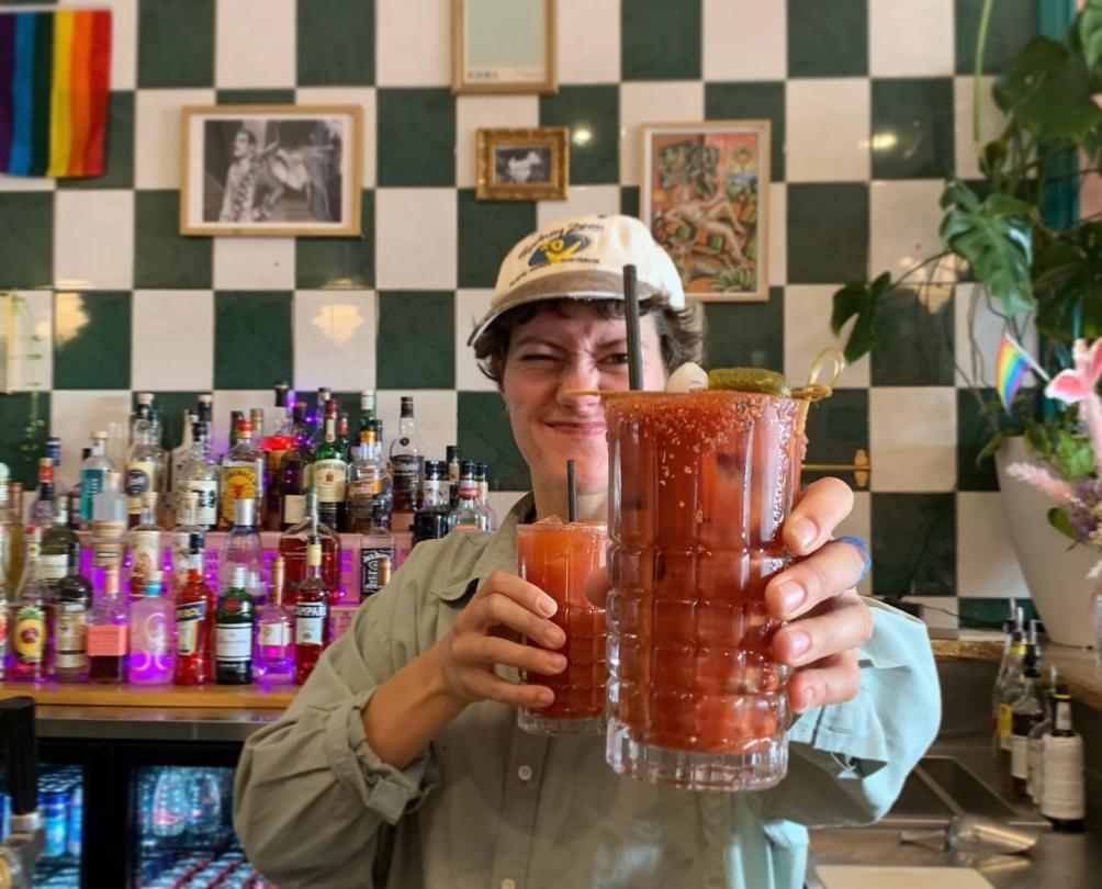 Bartender standing with cocktails in hand in front of a green and white checkered wall at The Flaming Galah