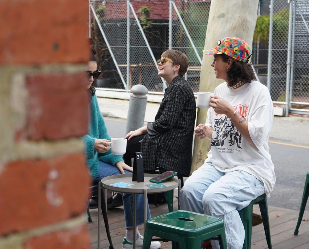 Women sitting on low stools outside Good Things enjoying a coffee