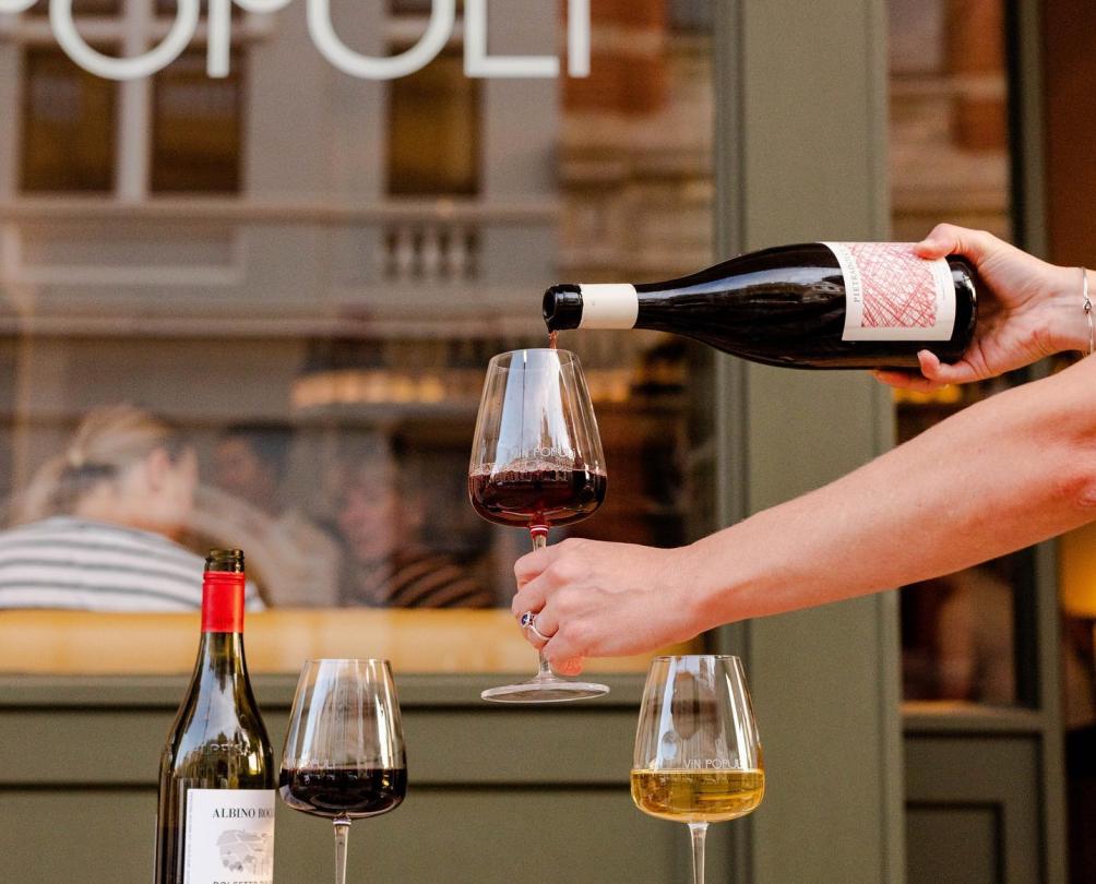 Red wine being poured in to a glass in front of a table set for two with bowls of pasta outside Vin Populi