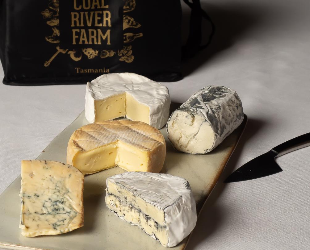 five soft cheeses on a board next to cheese knife and black Coal River Farm bag