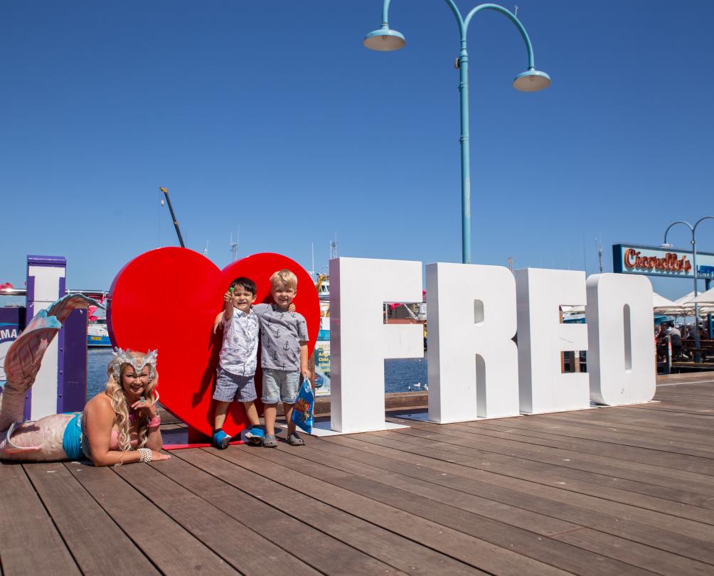Mermaid and two boys standing next to I HEART FREO sign at Fishing Boat Harbour