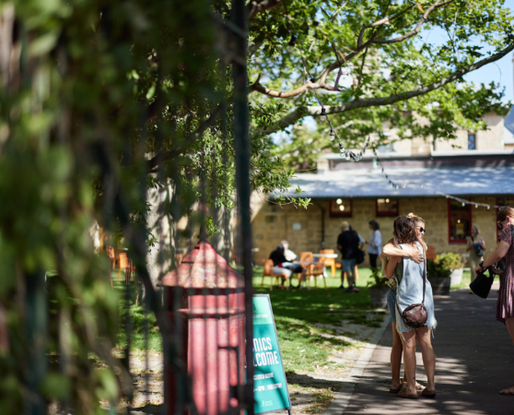 Friends greet each other with an embrace beyond FAC gates, near lush green lawns